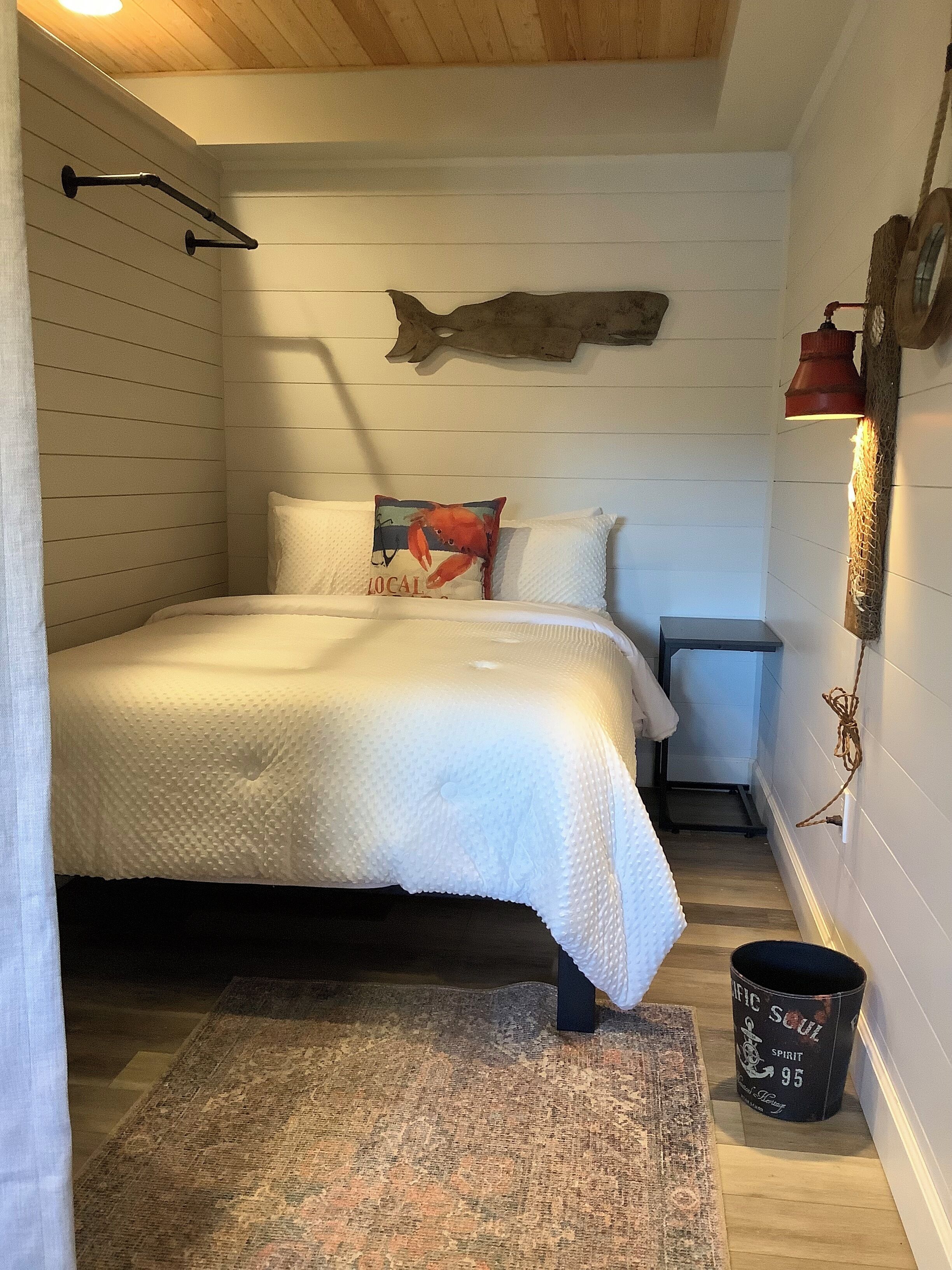 Une chambre à coucher avec un lit, des oreillers, un tapis, une table de chevet, une lampe fixée au mur et un poisson décoratif accroché au mur.