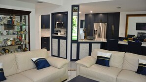 A modern living room with a beige sofa set, a coffee table, and a glass display cabinet filled with decorative items. - Relaxing Modern 4BR Family Oasis in Napes- 10 Min to Beach & Downtown Fun (Naples)
