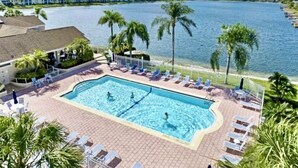 A swimming pool with lounge chairs and palm trees, surrounded by a body of water and a distant shoreline. - Relaxing Modern 4BR Family Oasis in Napes- 10 Min to Beach & Downtown Fun (Naples)