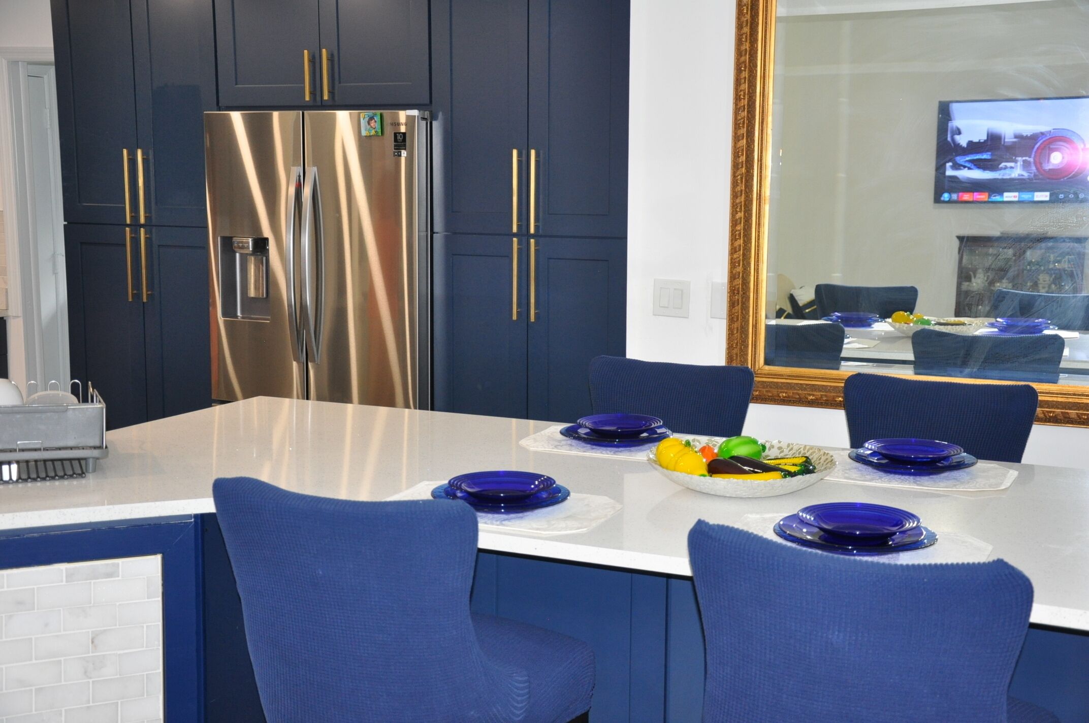 Una cocina moderna con armarios azul oscuro, un refrigerador de acero inoxidable y una zona de comedor con sillas y platos azules.