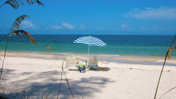 A beach with a striped umbrella, two beach chairs, and a bag on the sand. - Relaxing Modern 4BR Family Oasis in Napes- 10 Min to Beach & Downtown Fun (Naples)
