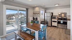 A modern kitchen with white cabinets, stainless steel appliances, and a wooden dining table with blue chairs. - Top Rated, Waterfront Condo at 19MM Amazing views! Prime location! Boat slip! (Osage Beach)