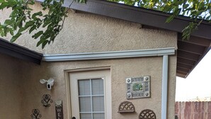 A patio with a door, a welcome sign, decorative wall pieces, and a table with chairs. - Cozy 1-bedroom apartment, WiFi, AC, Views! Wildlife! In charming Pahrump (Pahrump)