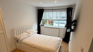 Ein Schlafzimmer mit Bett, einem Fenster mit Vorhängen, einem Heizkörper und Holzboden.