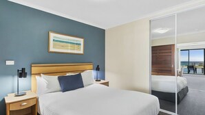 A hotel room with a bed, a nightstand, a lamp, a painting, and a sliding door to a balcony. - The Entrance Waterfront Apartment 505 (The Entrance)