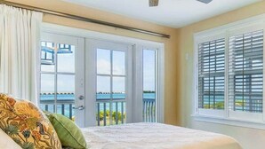 A bedroom with a bed, a ceiling fan, a view of the ocean through large windows, and a balcony with a railing. - Piece of Paradise located at Hawks Cay in Duck Key (Duck Key)