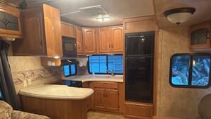 A compact RV kitchen with wooden cabinets, a stove, a microwave, and a refrigerator. - Fantastic RV with AC in Muskegon (Muskegon)
