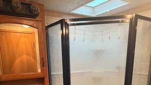 A bathroom with a wooden vanity, a sink, and a glass-enclosed shower. - Fantastic RV with AC in Muskegon (Muskegon)