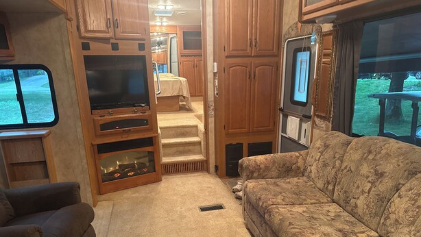 An RV interior with a sofa, TV, wooden cabinets, and a kitchen area. - Fantastic RV with AC in Muskegon (Muskegon)