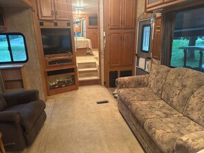 An RV interior with a sofa, TV, wooden cabinets, and a kitchen area.