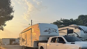A white truck towing a large recreational vehicle with a mountain design on the back, parked on a gravel surface. - Fantastic RV with AC in Muskegon (Muskegon)