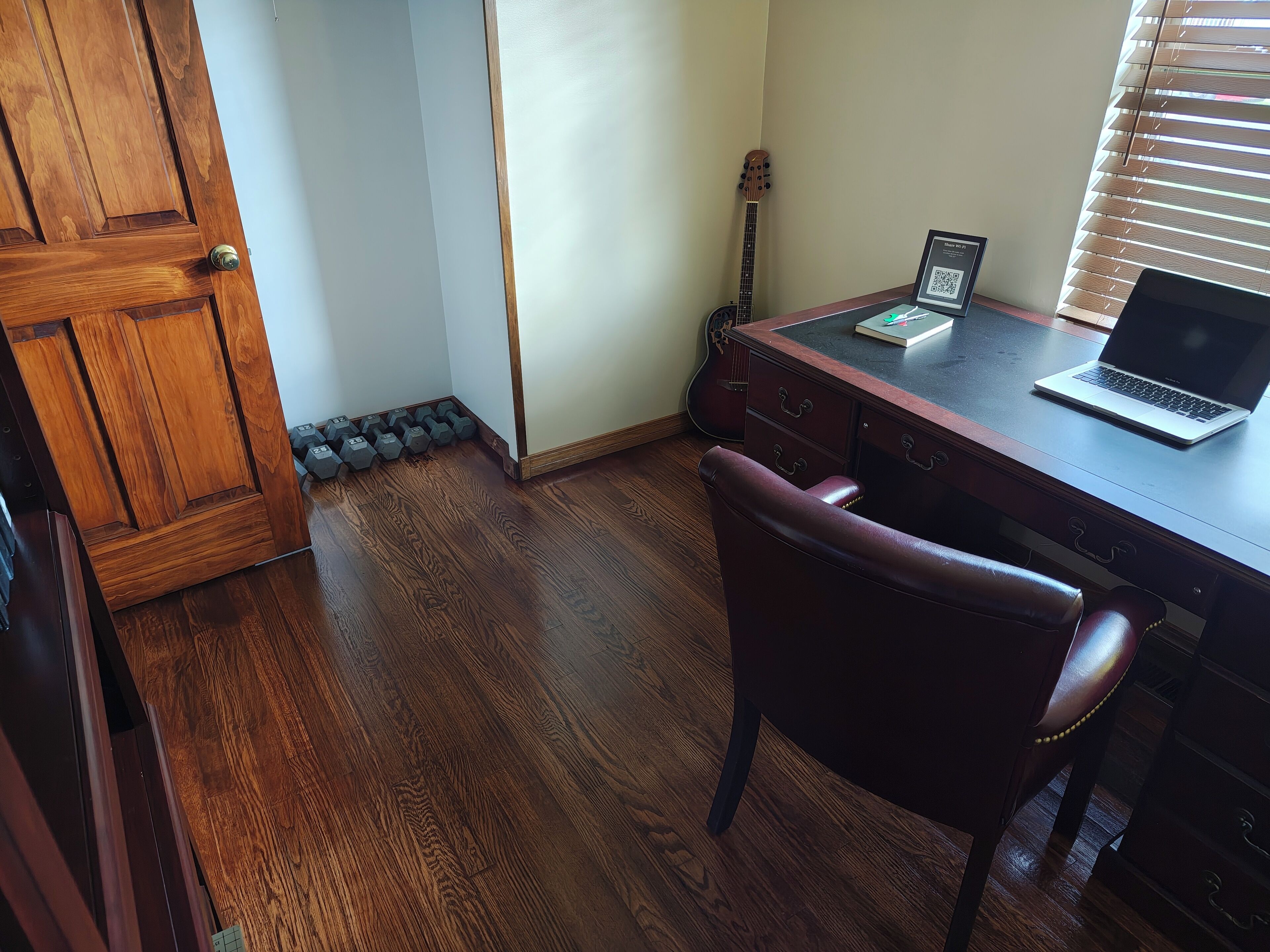 A room with a wooden desk, a laptop, a guitar, and a chair.