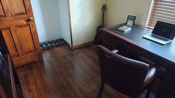 A room with a wooden desk, a laptop, a guitar, and a chair.