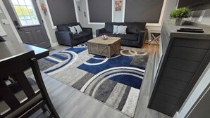 Un salon moderne avec deux canapés noirs, une table basse en bois et un tapis à motifs.