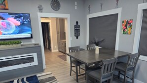 Une cuisine moderne avec des meubles gris, une table à manger avec des chaises, un téléviseur posé sur un meuble et une horloge au mur.