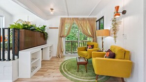 A modern living room with a wooden floor, yellow armchairs, a green rug, and a large window with curtains.