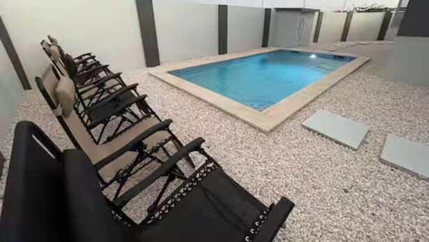 A rooftop pool area with a rectangular pool, black lounge chairs, and a white wall with vertical panels. - Island Escape Home in Noord, Aruba (Noord)