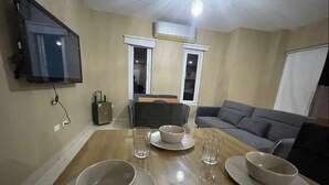 A dining area with a wooden table set for four, a television mounted on the wall, and a sofa in the background. - Island Escape Home in Noord, Aruba (Noord)