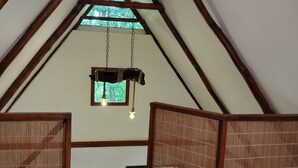 Ambiente interno in legno con soffitto spiovente, lampadario e vista su piante.