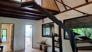 Ambiente spazioso con soffitto alto, travi in legno a vista, scala a chiocciola e vista sul verde circostante.