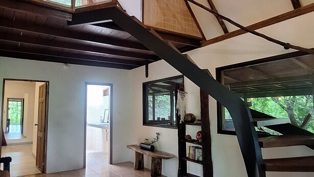Un intérieur spacieux avec de hauts plafonds, des poutres apparentes, un escalier en colimaçon et une vue sur la verdure environnante.