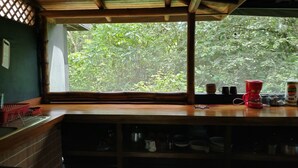 Une cuisine avec un comptoir en bois, une fenêtre donnant sur un paysage verdoyant et divers ustensiles de cuisine.