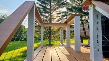A wooden deck with a pergola structure, surrounded by trees and a grassy area.