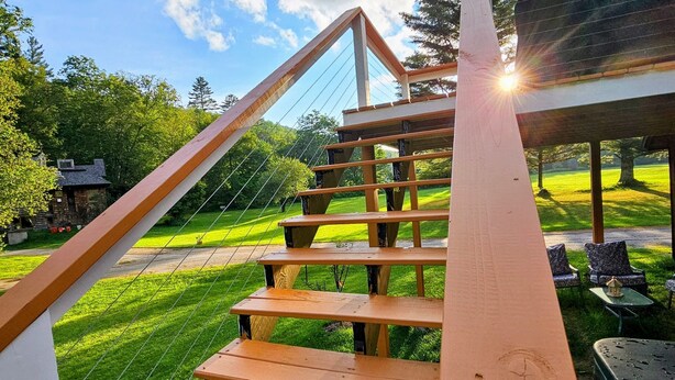 A wooden staircase leading to a covered outdoor area with a view of a green lawn and trees. - Cozy cabin >> Hottub, WiFi, AC. Easy access to outdoors activities year around (Hancock)