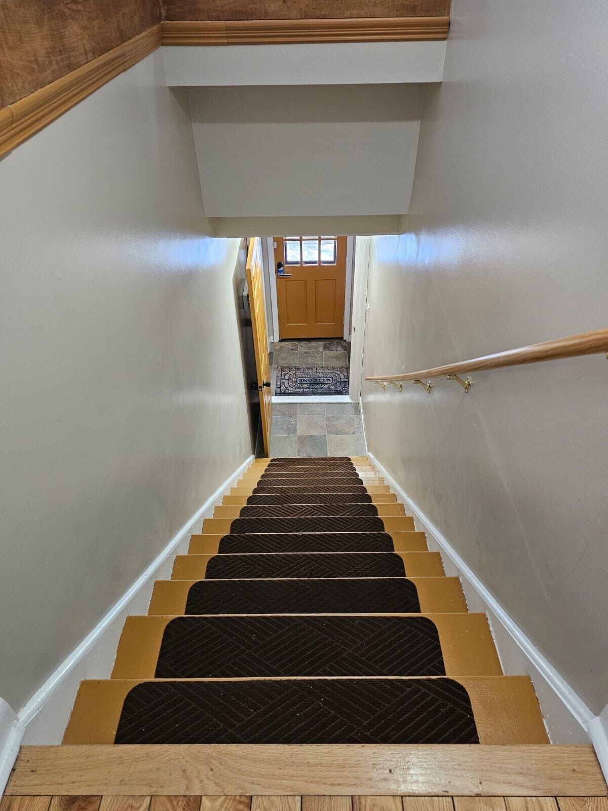 A wooden staircase with a handrail, leading to a door with a window above it.