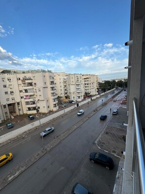 A multi-story residential building with balconies, a street with cars, and a clear sky. - S+1 in a new residence (Tunis)