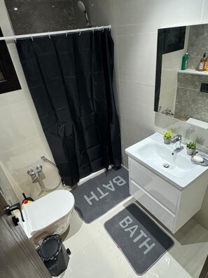 A modern bathroom with a white sink, a black shower curtain, and a mirror above the sink. There are two black bath mats with the word "BATH" on them. - S+1 in a new residence (Tunis)