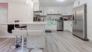 Une cuisine moderne avec des meubles blancs, un réfrigérateur en acier inoxydable et un coin bar équipé de tabourets.