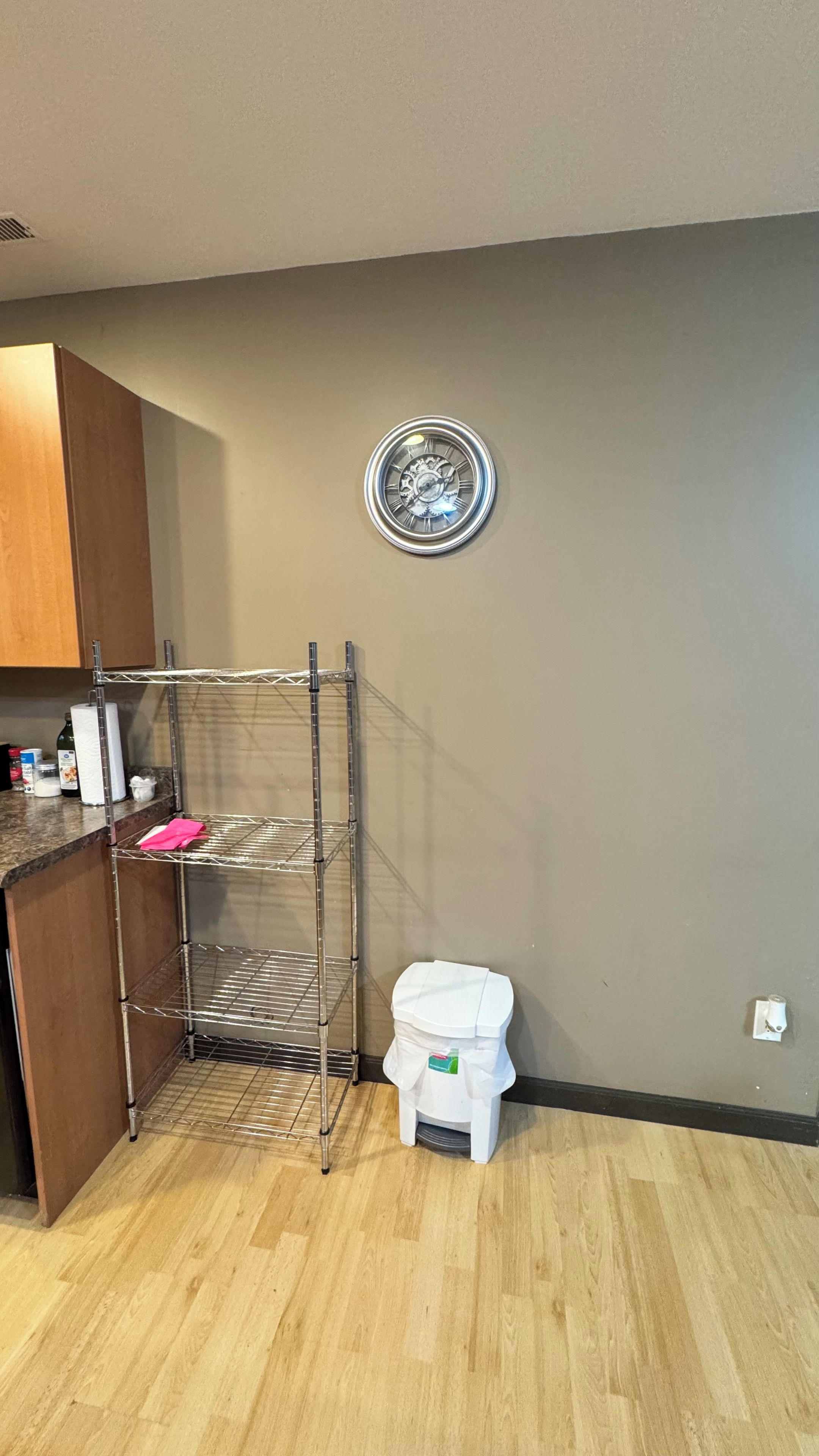 A kitchen with a metal rack, a toilet, and a wall clock.