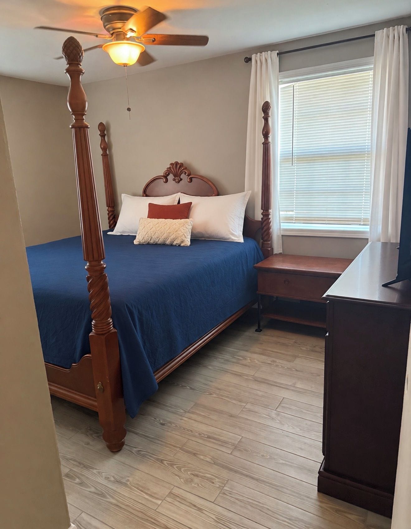 Une chambre à coucher avec un lit à baldaquin, un ventilateur de plafond, une fenêtre avec des stores et un bureau en bois.