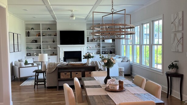 A spacious living area with a wooden dining table, comfortable seating, a TV, and a large window providing natural light.