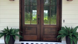 A double wooden door with glass panels, flanked by two lantern-style lights, and two potted ferns on either side.