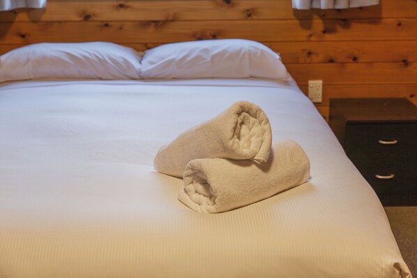 A neatly made bed with white linens and two folded towels on the bed.