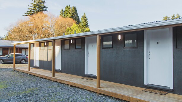A row of single-room cabins with a wooden deck in front, numbered doors, and a car parked outside. - The Turoa Lodge Ohakune (Ohakune)