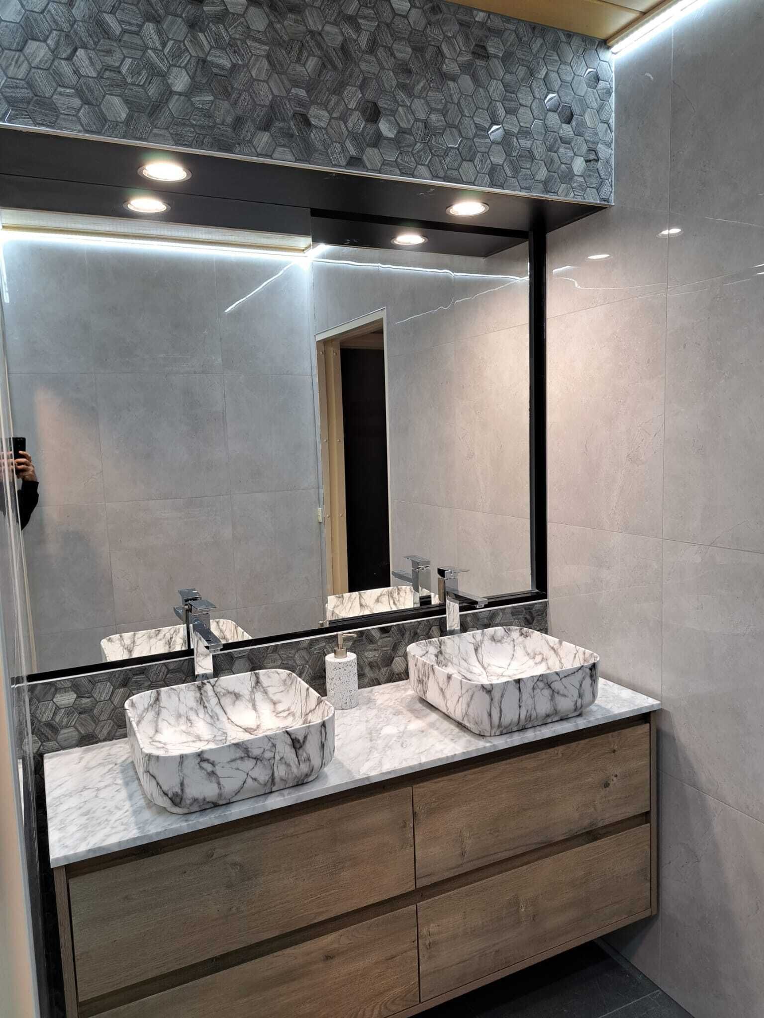 A modern bathroom with two marble sinks, a large mirror, and a wooden vanity.