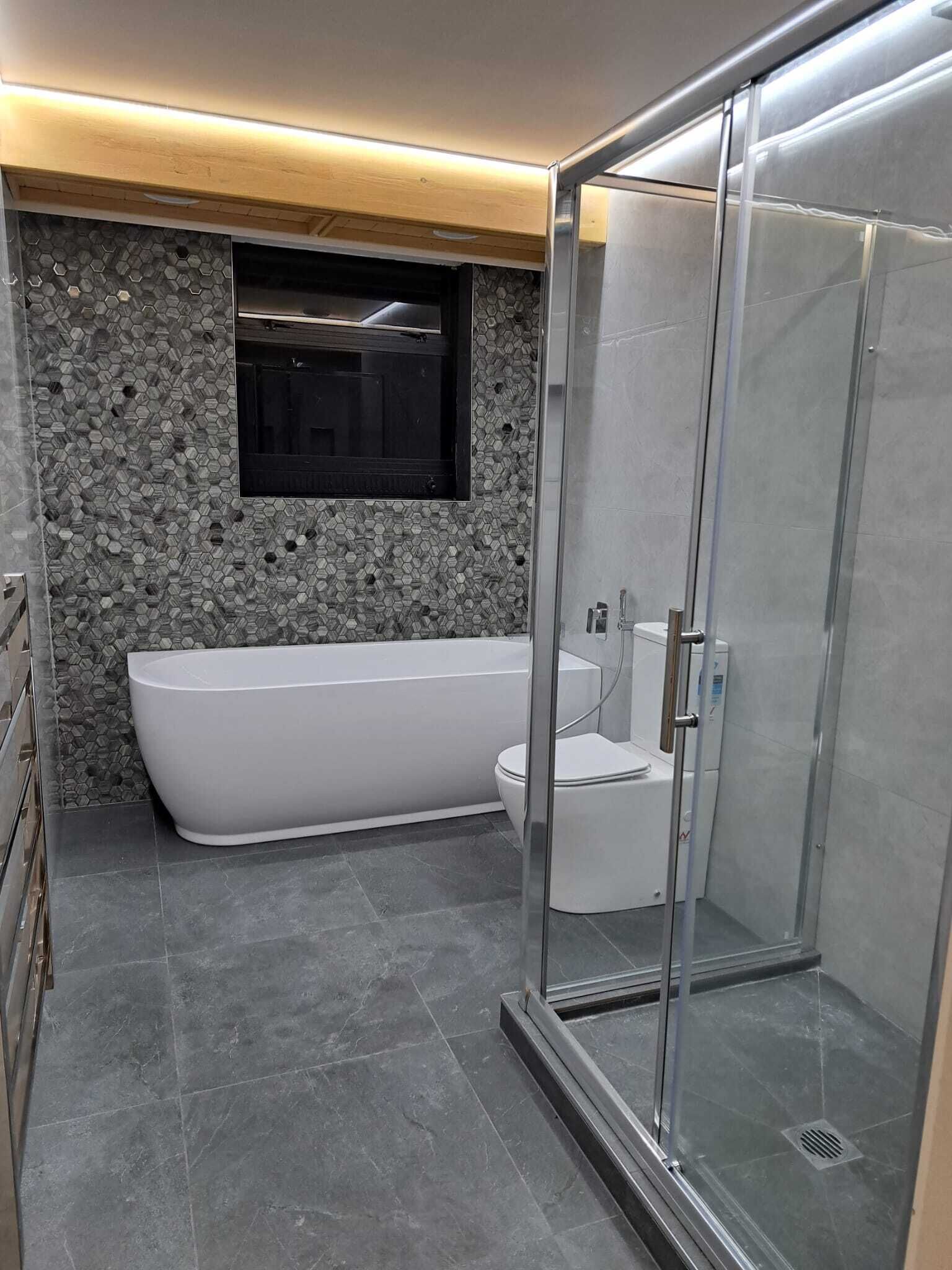 Uma casa de banho moderna com uma banheira independente, um chuveiro com divisória de vidro e um revestimento de parede com padrão de pedra.