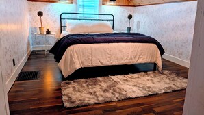 A cozy bedroom with a wooden ceiling, a bed with a white and dark-colored duvet, a fluffy rug, and two bedside lamps. - Teton Heritage House | Yellowstone Central Hub | Magical Tree (Teton)