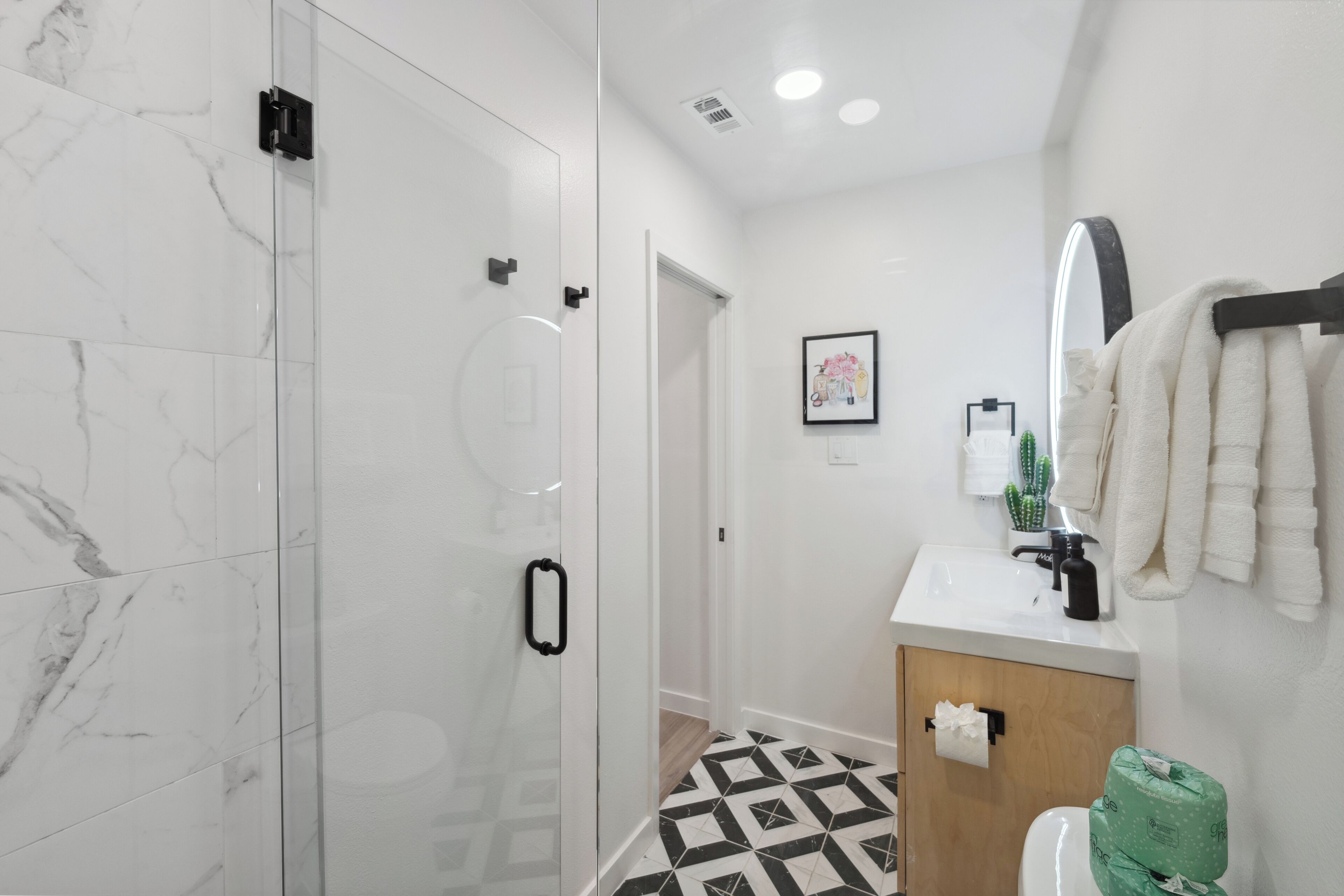 A modern bathroom with a glass shower enclosure, a sink with a mirror, and a patterned floor.