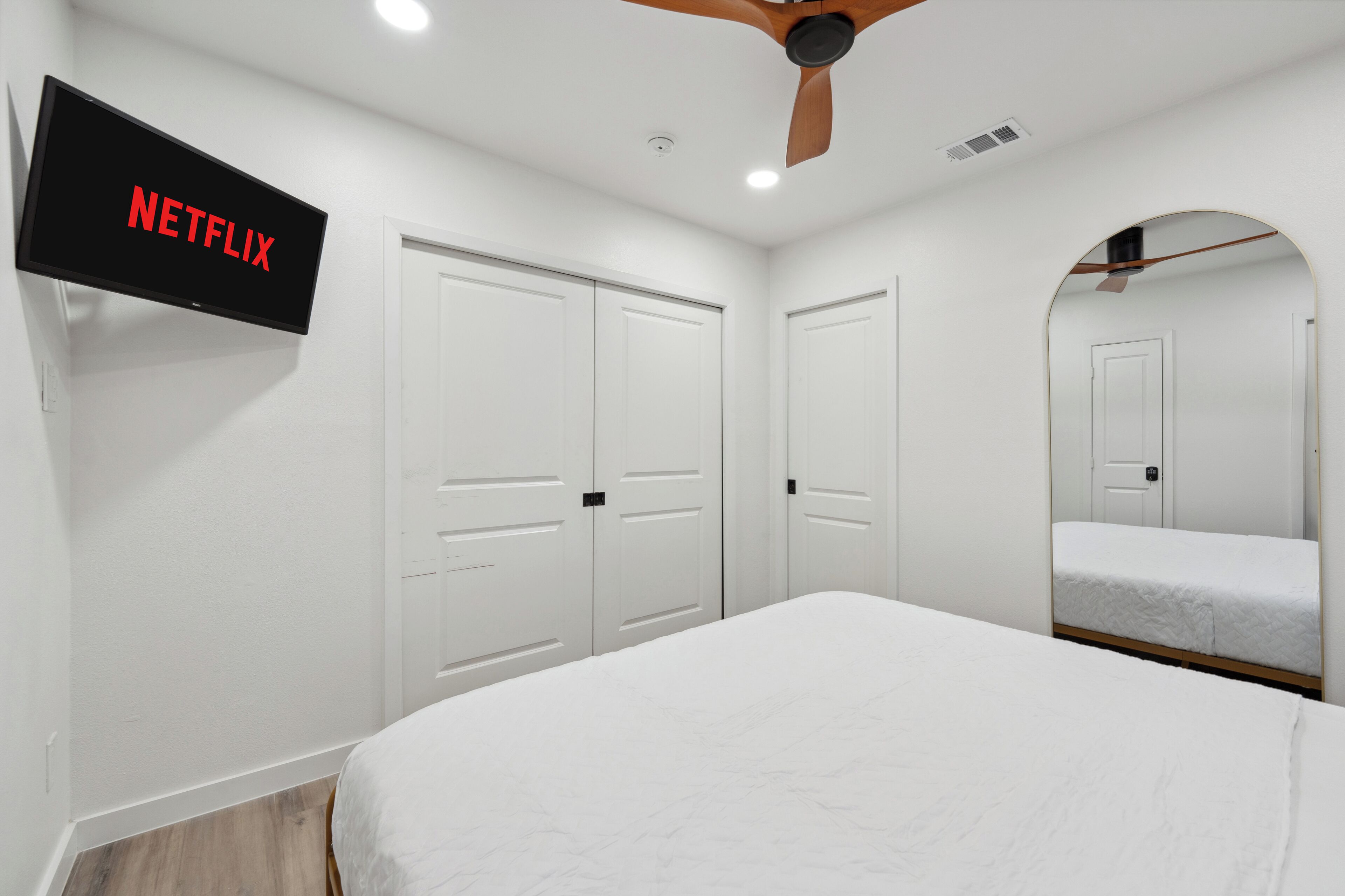 A bedroom with a bed, a TV mounted on the wall, and a ceiling fan.