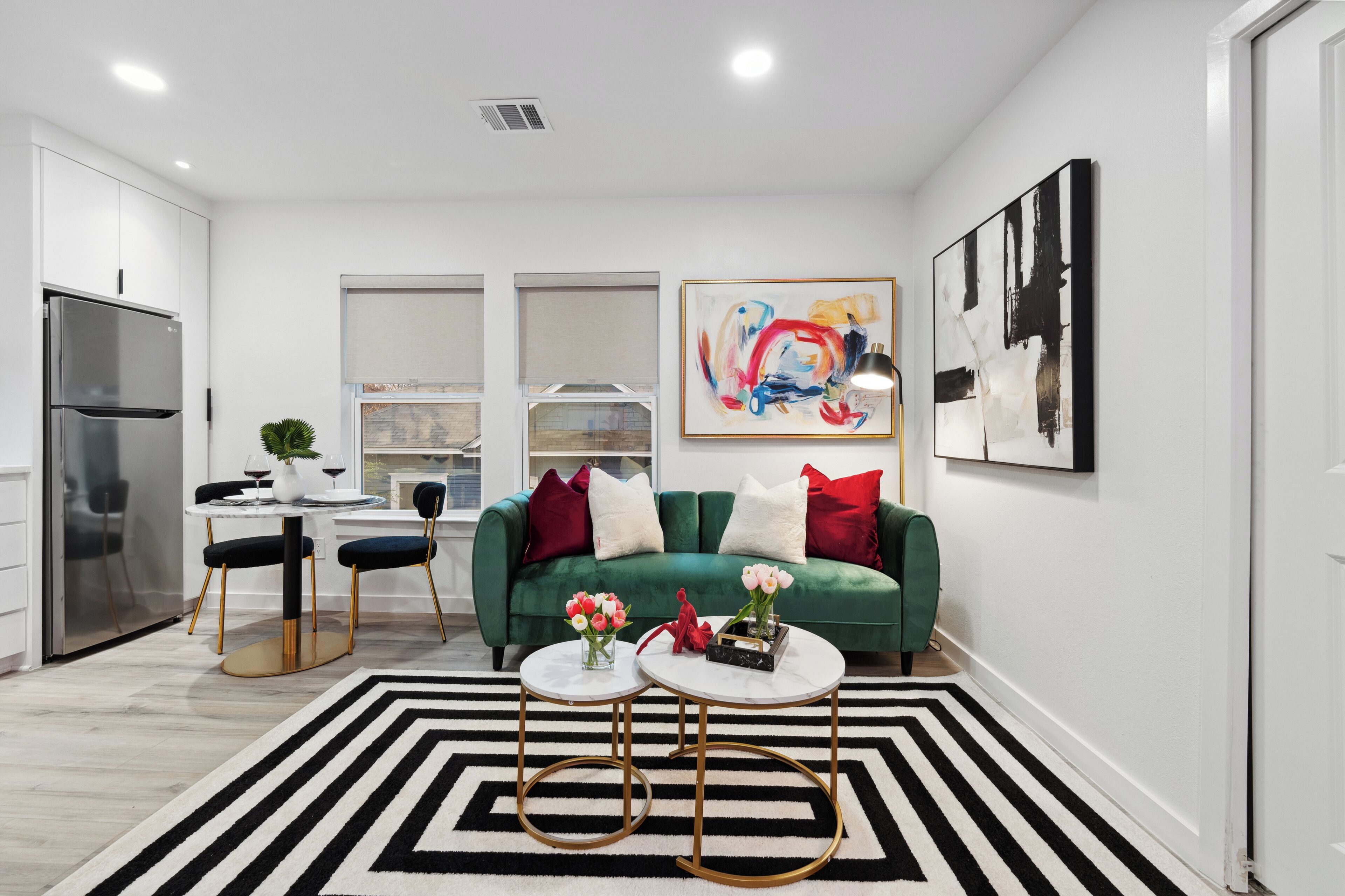 Una sala de estar moderna con un sofá verde, dos mesas redondas blancas y un tapete a rayas negras y blancas.