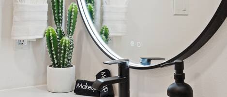 A bathroom with a white sink, a black faucet, a mirror, and a potted cactus.