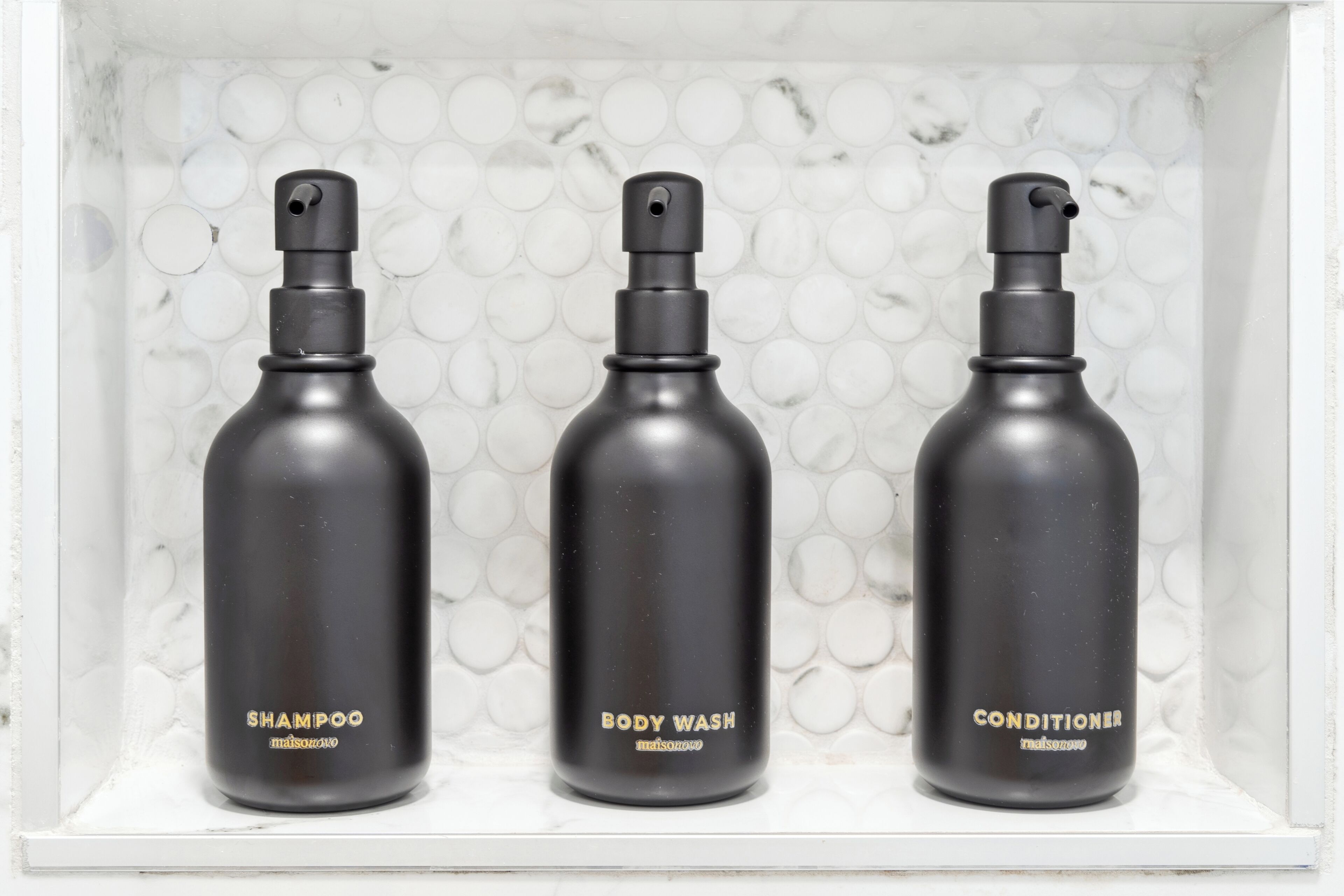 Three black bottles of shampoo, body wash, and conditioner in a white shelf.