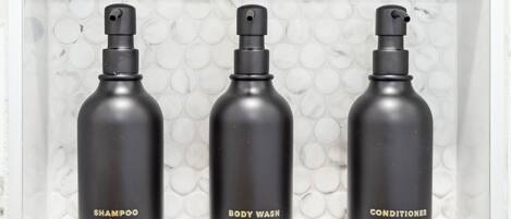 Three black bottles of shampoo, body wash, and conditioner in a white shelf.