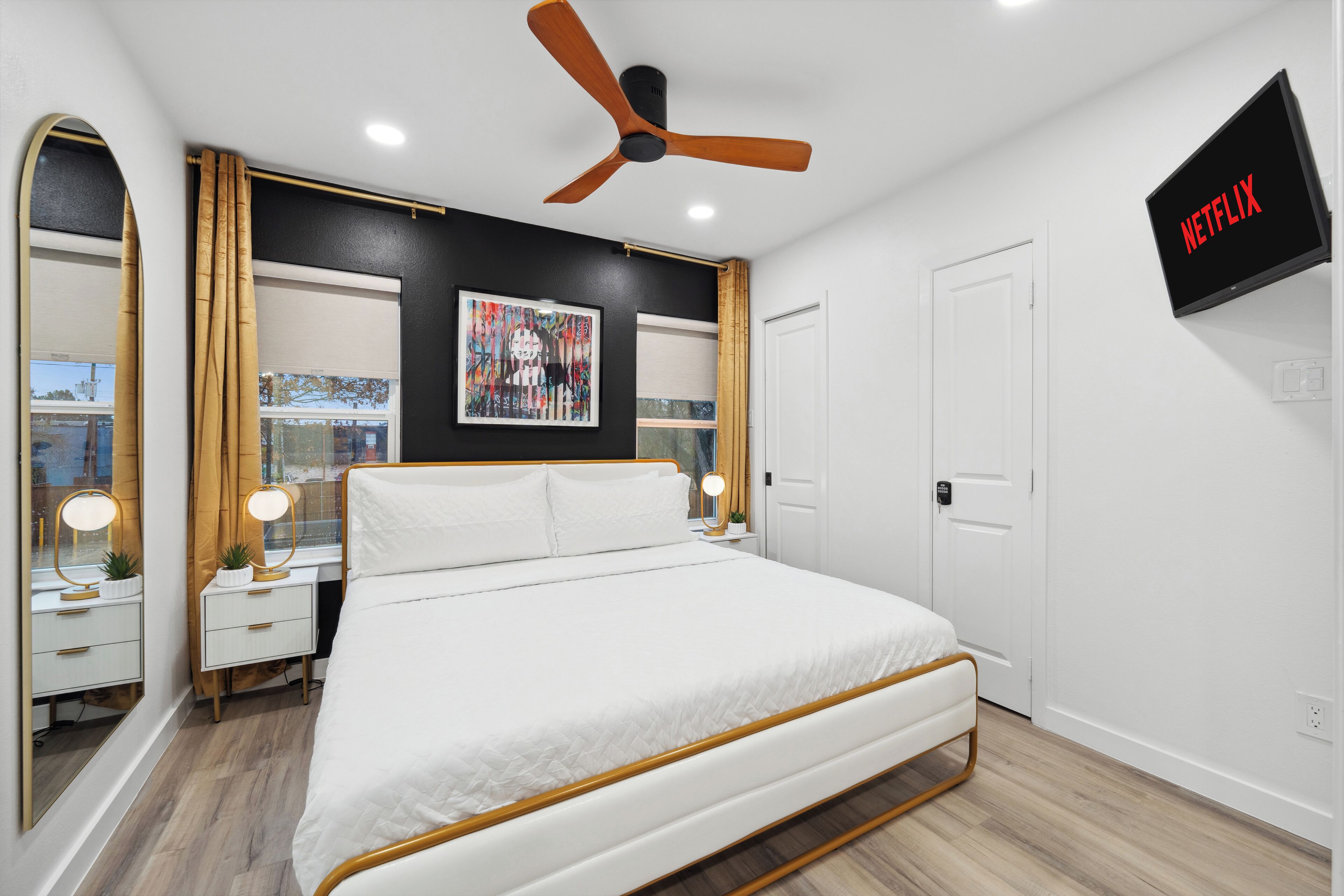 Une chambre moderne avec un lit, des tables de chevet, un ventilateur de plafond, une télévision et une fenêtre avec des rideaux.