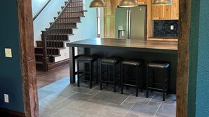 A kitchen with a central island, bar stools, wooden cabinets, and a staircase leading to another level. - A Peaceful Driftless Farm Stay Awaits Near A Trout Stream (Muscoda)