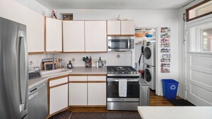 Een kleine keuken met witte kastjes, een roestvrijstalen koelkast, een magnetron, een oven en een wasmachine.